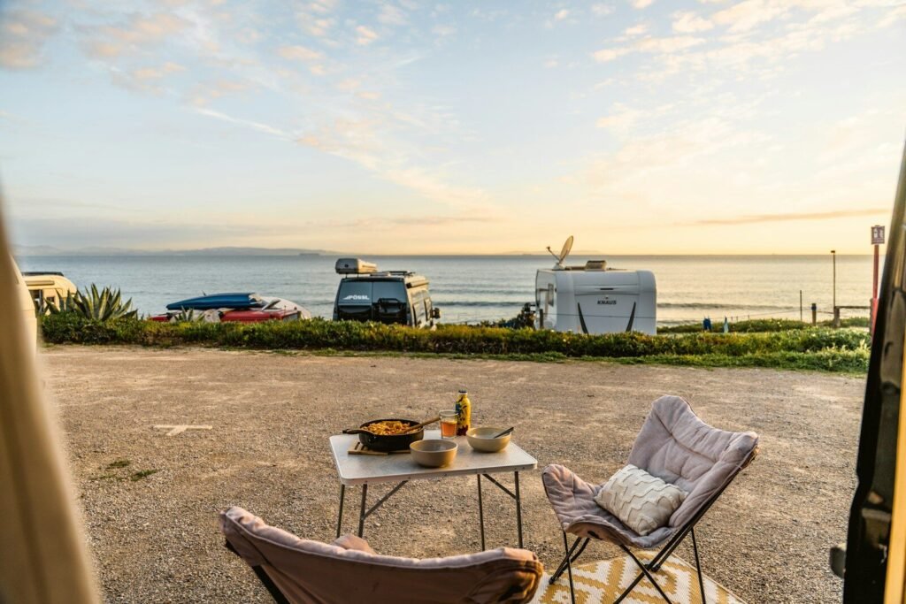 Campervans parked by the sea with outdoor dining setup.